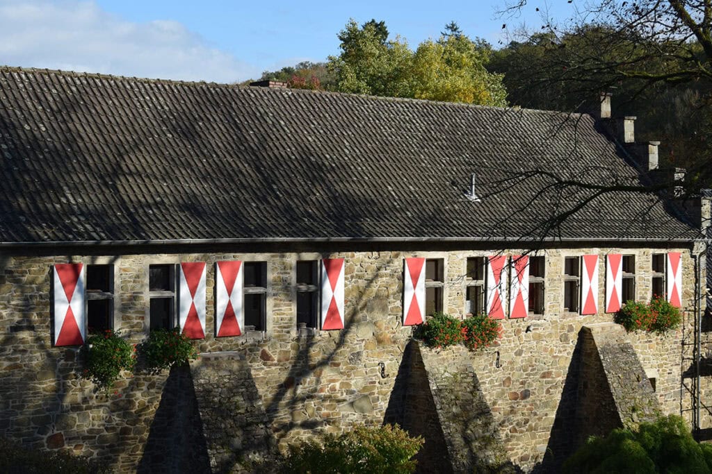 Steingebäude mit rot-weißen Fensterläden und Blumenkästen